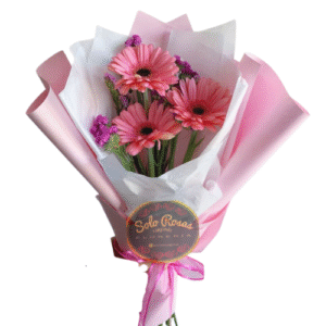 Ramo de tres gerberas rosadas con follaje decorativo y envoltorio rosa