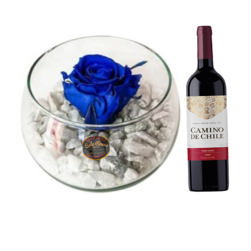 Rosa eterna azul presentada en pecera de vidrio decorativa acompañada de botella de vino